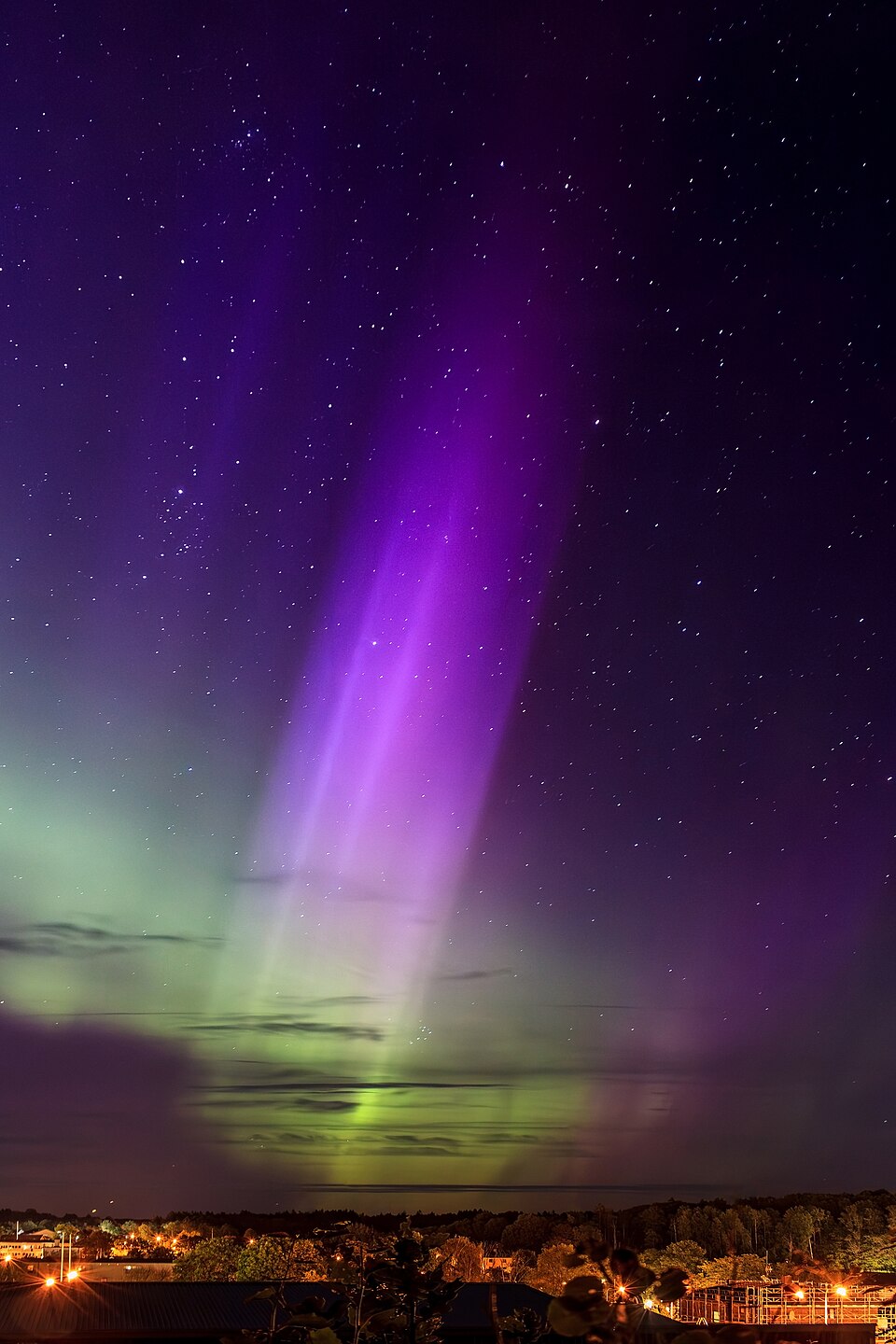 Multicoloured aurora pillar over a dark night landscape